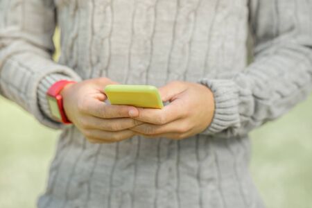 Online communication. Guy in warm grey sweater actively messaging on a smartphone while having pleasant walk outsideの写真素材