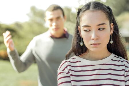 Upset dark-haired woman being tired of her jealous boyfriend while she expressing emotions on the streetの写真素材