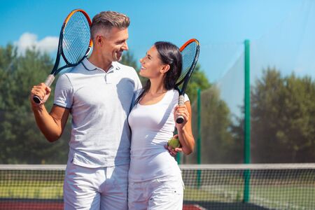 Good-looking happy couple holding rackets while loving tennis greatlyの写真素材