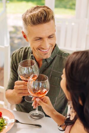 Husband smiling. Handsome husband wearing checked shirt smiling while drinking wine with wife