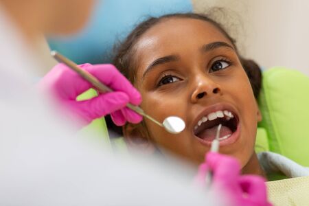 Routine dental checkup. Closeup portrait of a cute young girl sitting with an open mouth in front of a dentist examining herの写真素材