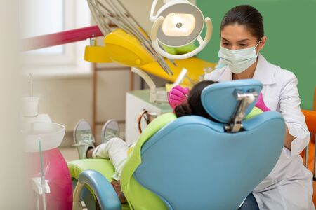Focused doctor. Concentrated dark-haired woman doctor leaning over her young patient sitting in a dentists chairの写真素材