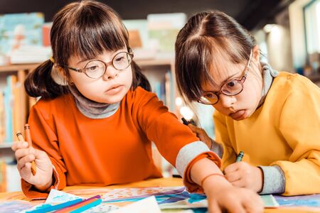 Having developing classes. Curious dark-haired girl in eyeglasses taking new color of pencil while...