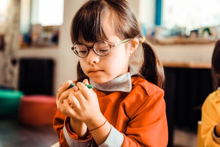 Checking new pencils. Interested little kid with two ponytails being focused on colorful crayons while wearing orange sweatshirtの写真素材