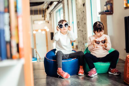 Calm young children. Girls with down syndrome spending time together in developing school and trying on stylish sunglassesの写真素材