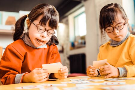 Card with red letters. Smiling girl in eyeglasses sitting with her serious sister and learning alphabetの写真素材