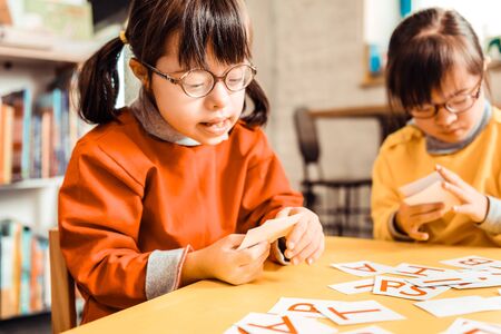 Learning process. Concentrated little student carrying bunch of card with letters while learning...