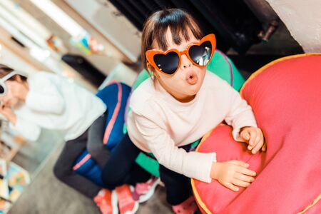 Showing new sunglasses. Active dark-haired kid being excited with her new stylish sunglasses while sitting on a chair bagの写真素材