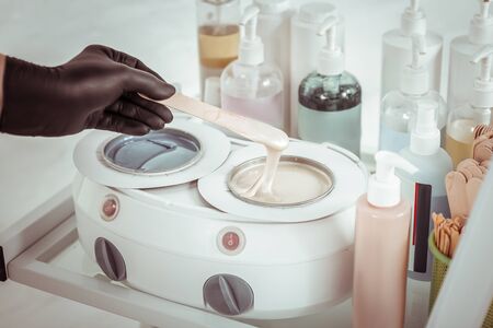 Master preparing. Experienced salon cosmetologist using special device for melting depilation wax for procedureの写真素材