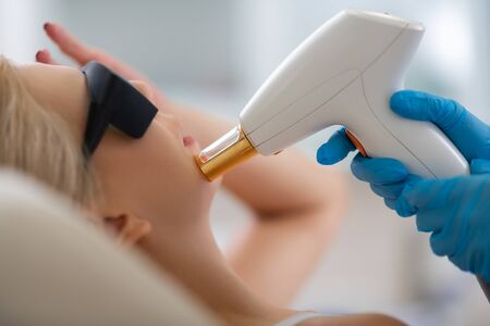 In the beauty salon. Hands of beautician giving laser skin treatment to her client lying on the couch.の写真素材