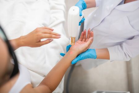 Taking care of hands. Hands of cosmetologist wearing rubber gloves holding hands of her client and...