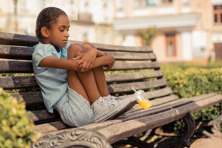 Sad teenager sitting on the bench alone and looking downwardsの写真素材