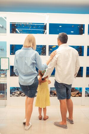 Parents hugging girl. Loving caring parents hugging girl while spending family weekend in aquariumの写真素材