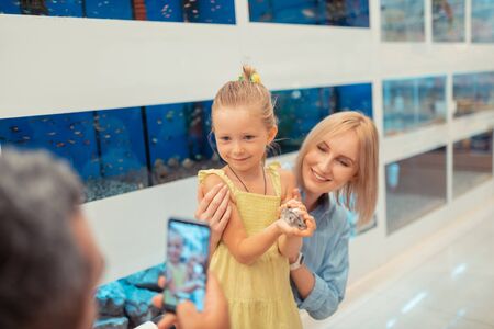 Photo of daughter. Daddy taking photo of daughter holding little hamster in hands while standing...