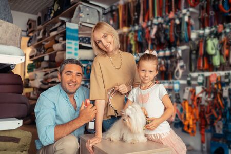 Happy family. Parents and girl feeling happy after finding dog collar for their white fluffy dog