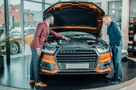 Knowing better. Interested man exploring the car under the capote with the help of a car dealer.の写真素材