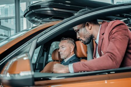Before the test-drive. Serious man that going to buy a car sitting inside it with a consultant of car salon near him.の写真素材