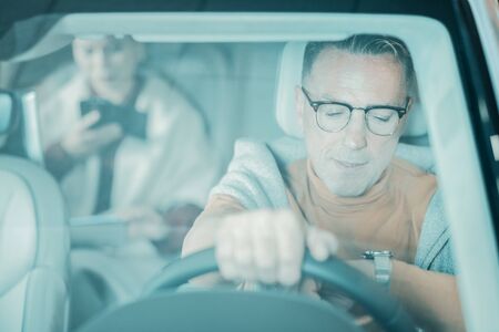 Trying to be on time. Handsome man sitting at the wheel looking at his wristwatch being a little...