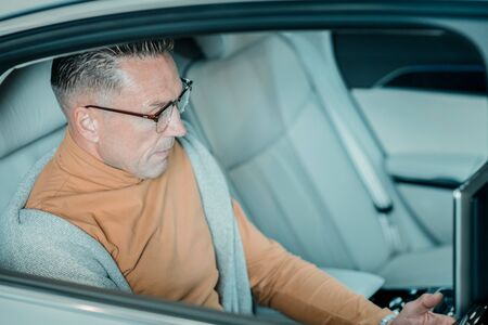 Thinking about work. Serious adult man wearing glasses sitting alone on the backseat of the car.