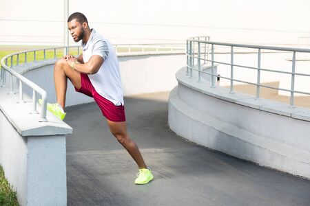 Stretching routine. Young dark-haired motivated male athlete in summer sportswear stretching his...