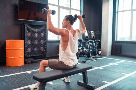 With weight. Attractive fit sportsman holding his hands up while having weight in them