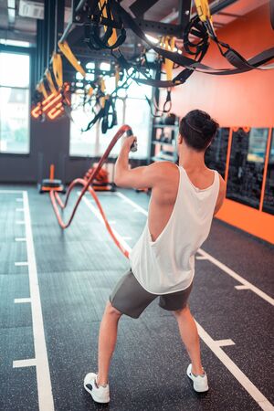 Sports workout. Nice young man holding ropes while having a crossfit training