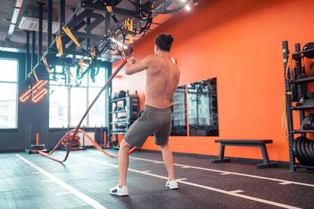Beautiful body. Fit well built man training with battling ropes while working on his shape