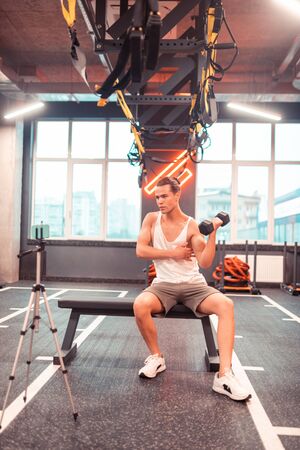 Repeat after me. Serious young man performing an exercise while conducting an online lesson for his...