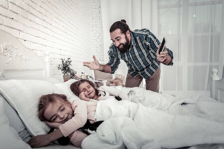 Happy and smiling dad showing his daughters the alarm in the morningの写真素材