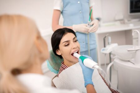 Thinking of new smile. Beautiful thoughtful woman opening her mouth getting dental treatment with specialtools in dentists office.の写真素材