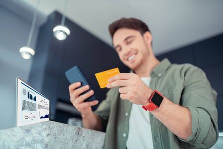 Shopping online. Close up of man wearing smart watch holding bank card while shopping online