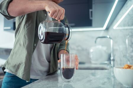 Coffee time. Close up of man wearing khaki shirt pouring coffee in the morning