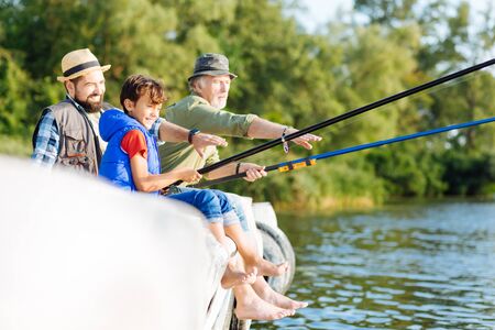 Boy feeling happy. Handsome dark-haired boy feeling happy while fishing with father and grandfather