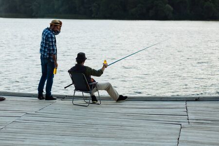 Fishing near river. Father and son feeling happy while enjoying evening while fishing near riverの写真素材