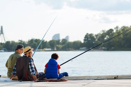 Dad and granddad. Boy feeling memorable while fishing with dad and granddad near the riverの写真素材