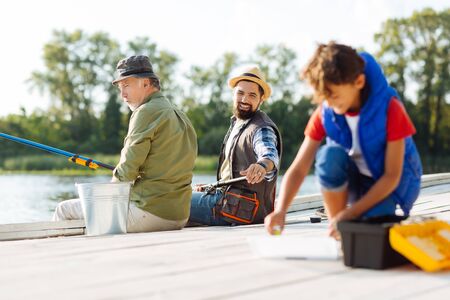 Find fishing hook. Bearded father asking his son to find fishing hook while having family fishing