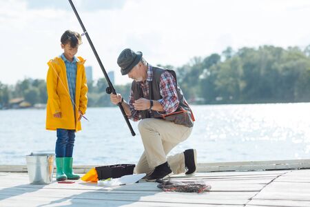 Preparing for fishing. Cute boy watching his grandfather preparing for fishing in the morningの写真素材