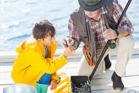 Taking sea line. Close up of dark-haired grandson taking sea line while fishing with grandfatherの写真素材