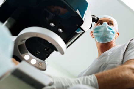 Low angle of an adult male doctor wearing a mask while standing near the microscopeの写真素材