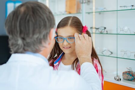 Excited child. Nice happy girl smiling to her doctor while being excited about her new eyeglassesの写真素材