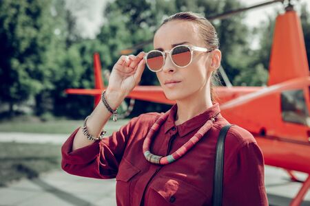 Wearing sunglasses. Elegant businesswoman wearing sunglasses and stylish accessories standing near helicopterの写真素材