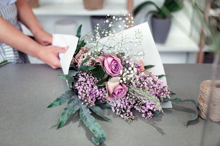 Girl being concentrated. Woman working as florist and wrapping bouquet of spring flowers in white piece of paperの写真素材