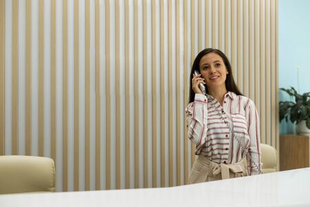 Welcome here. Cute brunette girl keeping smile on her face while talking per telephoneの写真素材