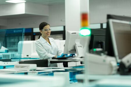 Well done. Pleased brunette girl keeping smile on her face while working in laboratory