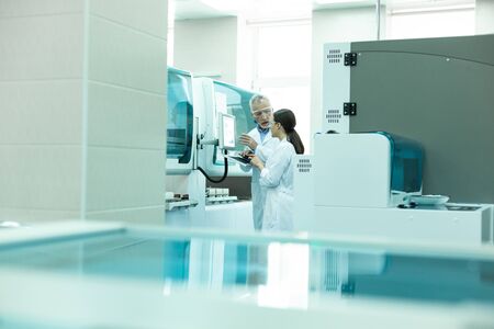 Modern lab. Serious bearded medical worker wearing protective glasses while demonstrating equipmentの写真素材