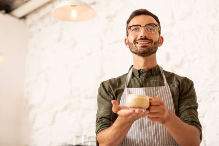 Cup of coffee. Smiling successful businessman owning cafe holding cup of coffee with milkの写真素材