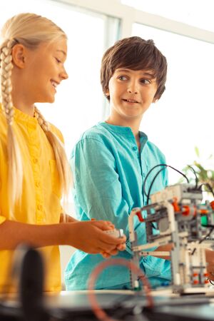 Science lesson. Smiling boy and girl standing together near the model built out of construction set and discussing their school science project.の写真素材