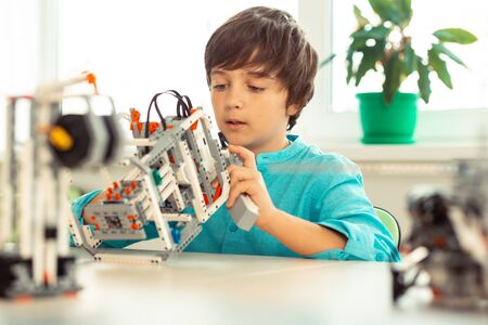 Smart school. Concentrated schoolboy sitting at the desk working with complicated construction set at the lesson.の写真素材