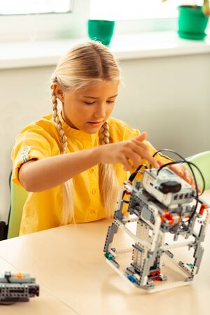 Technical school. Concentrated girl sitting at her science lesson making and turning on robot using...