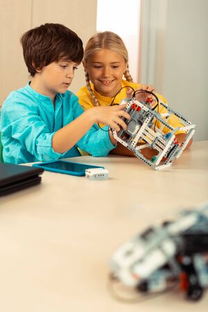 Little constructors. Two concentrated enthusiastic schoolchildren building a robot together during...
